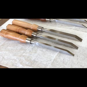 May include: Four wood handled chisels with metal blades. The blades are all the same length and have a beveled edge.