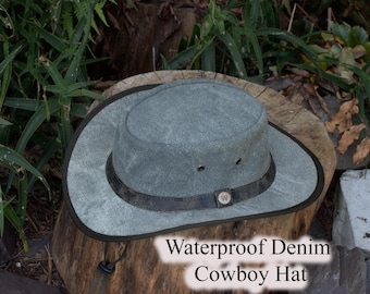 May include: A gray waterproof denim cowboy hat with a dark brown leather band and a small wooden button. The hat is sitting on a tree stump, with the text "Waterproof Denim Cowboy Hat" visible.
