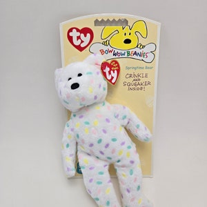 May include: White plush toy bear with a colourful confetti pattern. The bear is a Ty Beanie Baby with a tag that reads "Bow Wow Beanies" and "Springtime Bear". The tag also says "Crinkle and Squeaker Inside!"