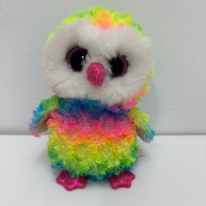 May include: A colorful rainbow owl plush toy with large black eyes and a pink beak. The owl is made of soft, fluffy material and has a white face.
