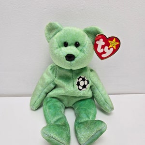 May include: Green Beanie Baby plush bear with a football on its chest. The bear has black eyes and a black nose. The bear is sitting on a white background. The tag reads "Beanie Babies" and "ty".