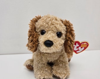 Puede incluir: Un perro de peluche marrón y beige con una etiqueta "Ty" roja y blanca. El perro tiene ojos marrones y una nariz negra.