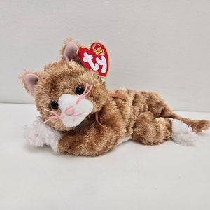 Op de afbeelding: Een bruin en wit tijgerkatten knuffel met een roze neus en witte pootjes. Het speelgoed ligt op zijn zij met zijn hoofd rustend op zijn poot. Het speelgoed heeft een rood en wit Ty Beanie Babies-label aan zijn oor.