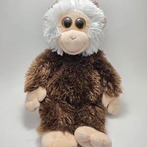 May include: A plush monkey toy with brown fur and a white-haired head. The monkey has large, round, brown eyes and a smiling face. Its hands and feet are a light tan color.