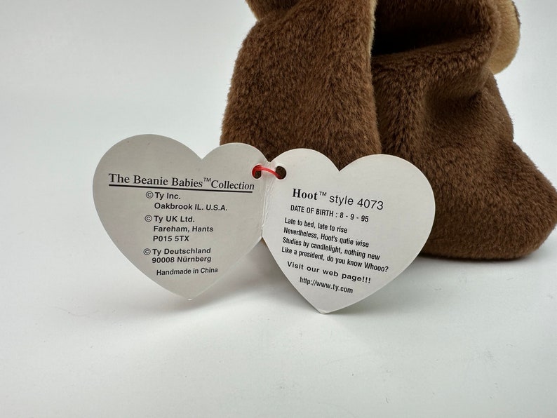 K&ouml;nnte beinhalten: Braunes Beanie Baby Pl&uuml;schtier namens "Hoot" mit einem herzf&ouml;rmigen Etikett. Das Etikett zeigt das Beanie Babies Logo und Informationen &uuml;ber das Spielzeug, einschlie&szlig;lich des Geburtsdatums: 8-9-95. Das Etikett enth&auml;lt auch den Text "Late to bed, late to rise. Nevertheless, Hoot's quite wise. Studies by candlelight, nothing new. Like a president, do you know Whooo? Visit our web page!!! http://www.ty.com"