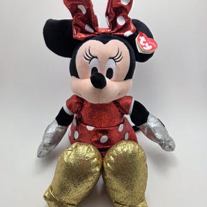 May include: A plush Minnie Mouse doll. The doll has a red dress and bow, both with white polka dots. It has black ears, a black nose, and silver gloves. The gold glittery shoes add a touch of sparkle.