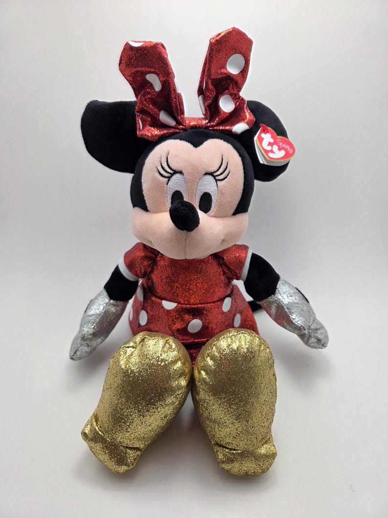 May include: A plush Minnie Mouse doll. The doll has a red dress and bow, both with white polka dots. It has black ears, a black nose, and silver gloves. The gold glittery shoes add a touch of sparkle.
