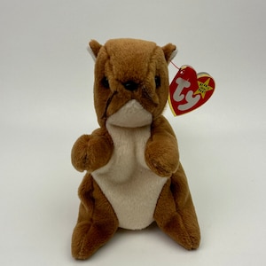 May include: A brown and white plush squirrel with a red Beanie Baby tag that says "Beanie Babies" and has a star on it.