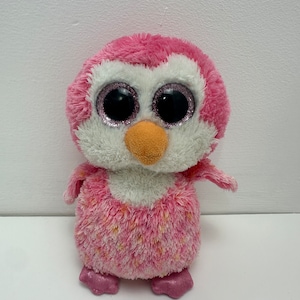 May include: Pink and white penguin plush toy with sparkly eyes. The penguin has a white belly and pink and white speckled fur.