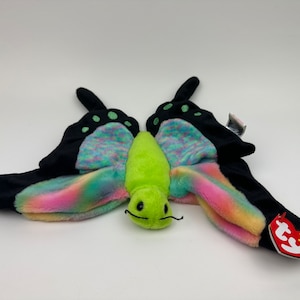 May include: A plush butterfly toy with black wings and rainbow-coloured accents. A green caterpillar toy is in the centre. The butterfly wings have black tips with green spots. A red tag with a heart is attached to the butterfly.