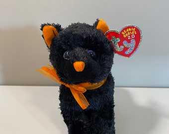 Puede incluir: Gato de peluche negro con orejas naranjas y una cinta naranja a juego alrededor del cuello. El gato tiene ojos morados y una pequeña nariz naranja. El gato es un Beanie Baby 2.0.