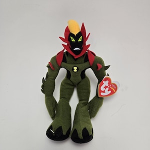 Könnte beinhalten: Grün-rotes Plüschtier eines Charakters mit gelber Haube und schwarzen Augen. Das Spielzeug hat ein Ty Beanie Babies-Etikett am Arm.