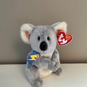 May include: Gray and white plush koala bear sitting with its arms crossed. The bear has a red Beanie Babies 2.0 tag attached to its ear. The bear also has a blue and yellow tag that says "Play Online!" and "Jouer en ligne!"
