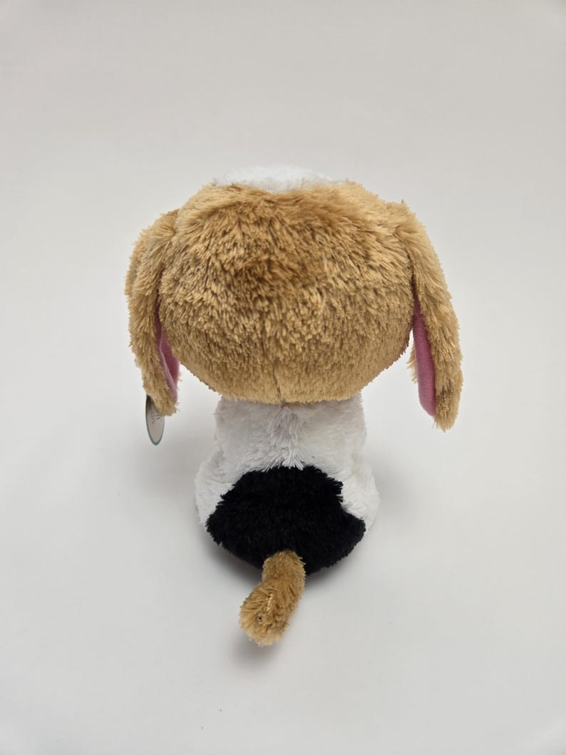 May include: A brown and white plush dog with pink ears sitting on a white background. The dog has a black spot on its back.