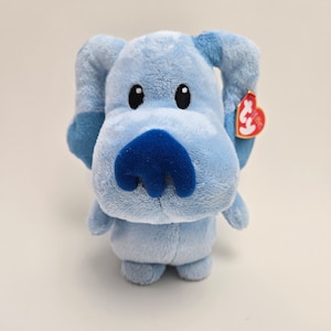 以下が含まれることがあります： 青い鼻と大きな目を持つ青いぬいぐるみ犬。おもちゃには赤い「Ty」タグが耳に付いています。