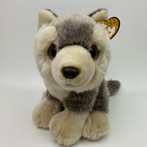 May include: A gray and white plush wolf with brown eyes and a black nose. The wolf is sitting with its paws tucked under its body. The wolf has a "Wild  Wild  Wild" Ty tag attached to its ear.