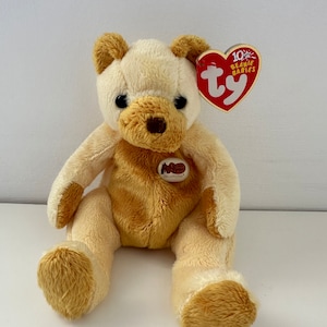 Peut inclure: Un ours en peluche Beanie Baby de couleur crème et brun clair avec une étiquette rouge Ty indiquant "10th Beanie Babies" et une étiquette brune indiquant "Old Country Store".