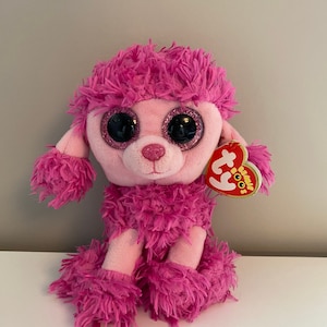 May include: A pink plush poodle toy with large, glittery eyes and a red heart-shaped tag. The poodle has fluffy, textured fur in shades of pink and a sweet expression. A fun and cuddly stuffed animal.