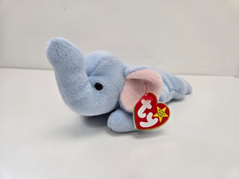 May include: A light blue plush elephant with a pink ear and a red Ty tag that says "Beanie Babies".