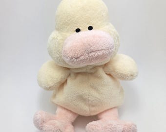 Può includere: Un giocattolo di peluche a forma di anatra gialla con piedi rosa e un becco rosa. L'anatra ha occhi neri e una texture morbida e soffice.