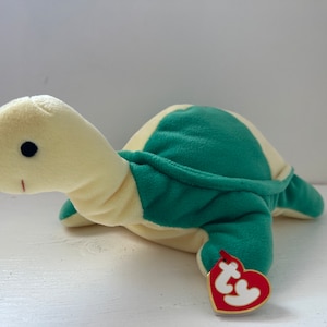 May include: A yellow and green plush turtle toy with a red and white "Ty" tag attached. The turtle has a small black eye and a stitched smile.