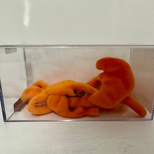 May include: A bright orange plush toy shaped like a crab in a clear plastic display case.