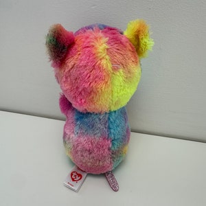 May include: A small, multi-colored plush toy with a tie-dye pattern. The toy has a pink glittery tail and a red heart tag with the word "ty" on it.
