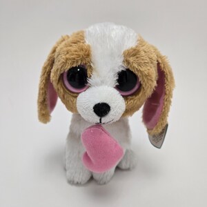 May include: A brown and white plush dog with large pink eyes and a pink heart in its paws. The dog is holding the heart in front of it.