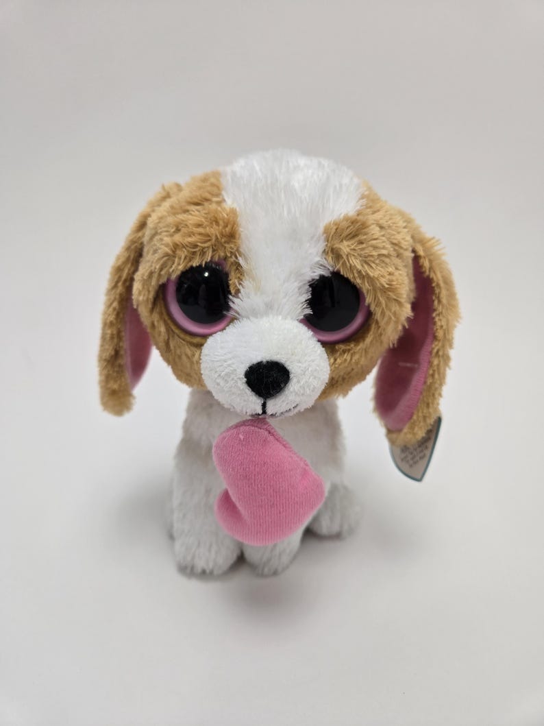 May include: A brown and white plush dog with large pink eyes and a pink heart in its paws. The dog is holding the heart in front of it.