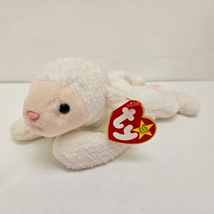 May include: A white plush lamb toy with a pink nose and ears, and black eyes. The lamb is lying down with its legs extended. A red heart-shaped tag is attached to the lamb.
