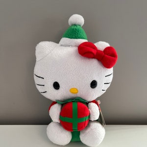 May include: A white plush Hello Kitty toy wearing a green Santa hat and holding a red and green gift box.