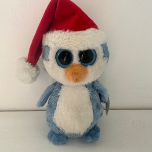 May include: A blue and white penguin plush toy wearing a red Santa hat. The penguin has large black eyes and a small orange beak.