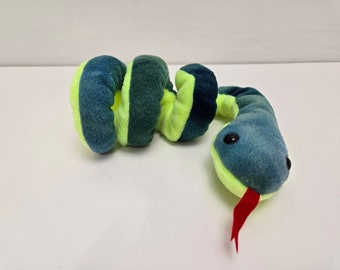 Pode incluir: Um brinquedo de pelúcia de cobra verde e amarelo com uma língua vermelha. A cobra está enrolada em uma espiral.