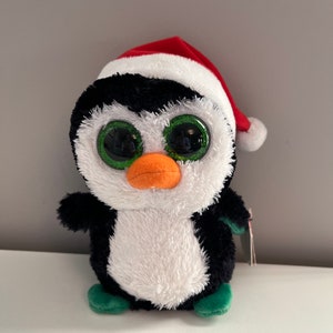 Puede incluir: Un juguete de peluche de pingüino blanco y negro que lleva un gorro de Papá Noel rojo con ribete blanco. El pingüino tiene grandes ojos verdes y un pico naranja brillante. El juguete tiene pies verdes.