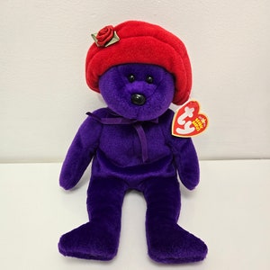 Pode incluir: Urso de pelúcia roxo Beanie Baby usando um chapéu vermelho com uma rosa no topo. O urso tem um nariz preto e olhos pretos. O urso tem uma etiqueta Ty presa ao seu braço direito.