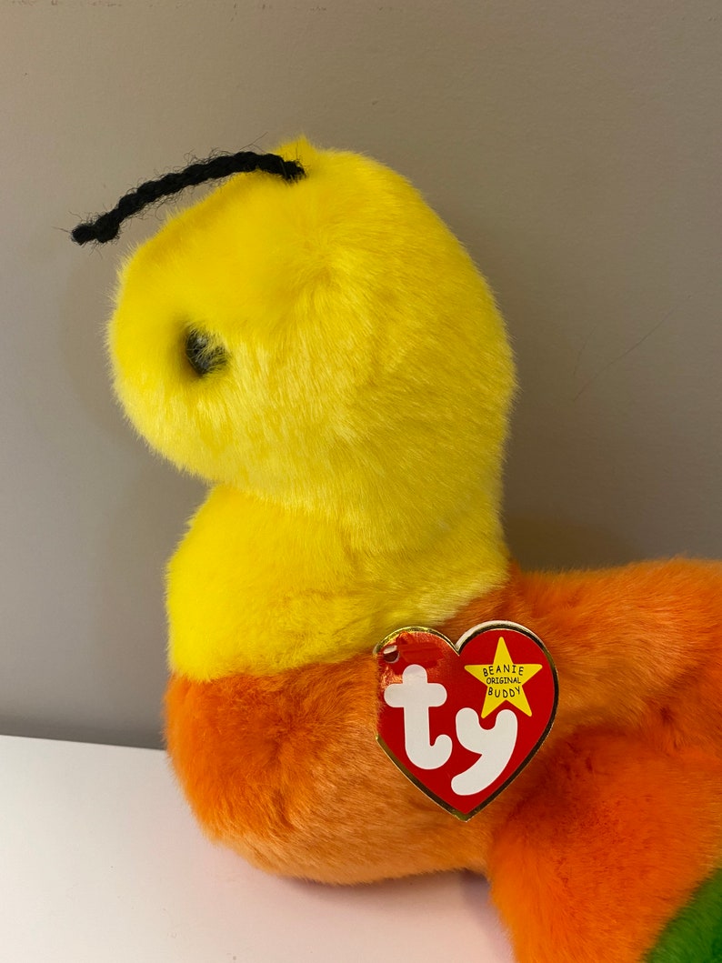 Op de afbeelding: Een gele en oranje gestreepte beanie baby met een zwarte garenantenne. De beanie baby heeft een rood Ty-label met de woorden "Beanie Original Buddy" erop.