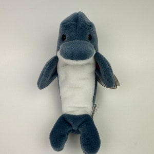 Puede incluir: Un juguete de peluche de delfín azul y blanco. El delfín tiene ojos negros y una barriga blanca.