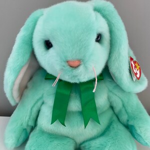 Puede incluir: Un conejito de peluche verde menta con largas orejas ca&iacute;das y un lazo de cinta verde. El conejito tiene ojos negros, bigotes rosas y una nariz rosa. Una etiqueta roja est&aacute; sujeta a la oreja.