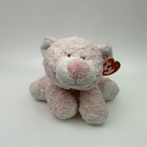 May include: A plush pink cat toy with a white muzzle and paws. The cat has a pink nose and brown eyes. A red and white tag is attached to the ear.