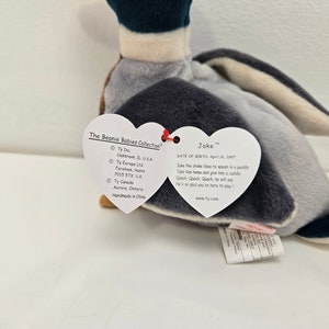 Pu&ograve; includere: Un giocattolo di peluche a forma di anatra grigio e blu di nome Jake della collezione Beanie Babies. L'etichetta dice "A Jake il germano reale piace sguazzare in una pozzanghera. Portalo a casa e dagli un abbraccio. Quack, Quack, Quack, dir&agrave;. &Egrave; cos&igrave; contento che tu sia qui per giocare."