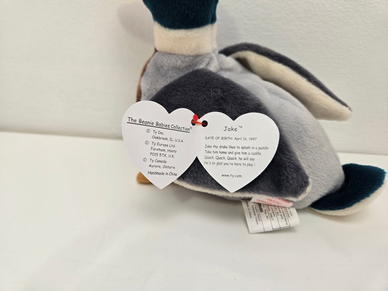 Pu&ograve; includere: Un giocattolo di peluche a forma di anatra grigio e blu di nome Jake della collezione Beanie Babies. L'etichetta dice "A Jake il germano reale piace sguazzare in una pozzanghera. Portalo a casa e dagli un abbraccio. Quack, Quack, Quack, dir&agrave;. &Egrave; cos&igrave; contento che tu sia qui per giocare."