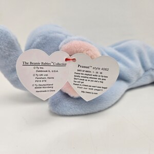 May include: A light blue Beanie Baby elephant named Peanut with a pink nose and a red heart-shaped tag. The tag includes the name Peanut, the style number 4062, and the date of birth 1-25-95. The tag also includes information about the manufacturer, Ty Inc., and the country of origin, China.