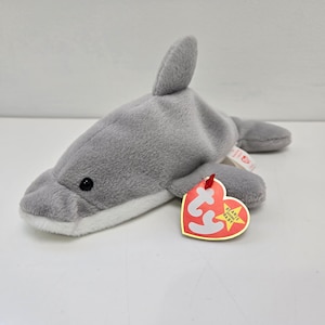 Puede incluir: Peluche de delfín gris en forma de beanie baby con una etiqueta Ty roja y blanca que dice "Beanie Babies" y "Baby".