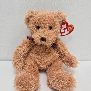 May include: A brown plush teddy bear with a red and black plaid ribbon around its neck. The bear has a Ty Beanie Babies tag attached to its ear. The tag is red with white text that reads "Original Beanie Babies".
