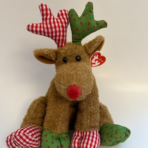 May include: A brown plush reindeer with red and white gingham and green star patterned fabric accents. The reindeer has a red nose and a Ty tag attached to its ear.