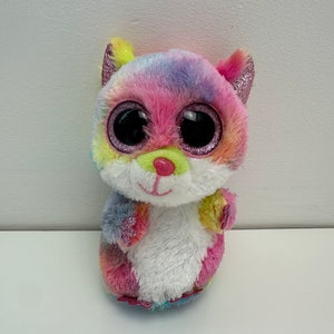May include: A colorful plush toy with large, glittery eyes. The toy is pink, blue, yellow, and green with a white belly. It has a cute, cartoonish face.