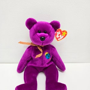 May include: Purple Beanie Baby plush toy with a gold ribbon and a Ty tag. The bear has a small globe on its chest with the text "Earth 1997".
