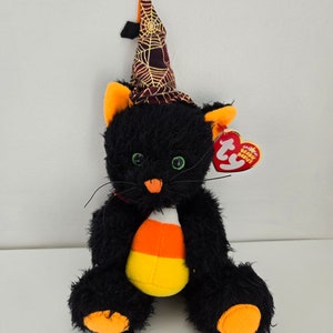 May include: Black plush cat wearing a witch hat with a spiderweb design and holding a candy corn. The cat has green eyes and orange paw pads. The tag reads "Ty Beanie Babies".