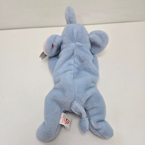 May include: A light blue plush elephant with a pink nose and ears. The elephant is lying on its back with its legs in the air. The tag on the elephant reads "Ty Inc. Beanie Babies -  Collection".