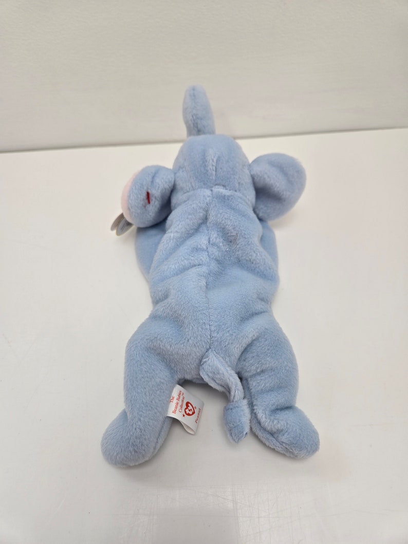 May include: A light blue plush elephant with a pink nose and ears. The elephant is lying on its back with its legs in the air. The tag on the elephant reads "Ty Inc. Beanie Babies -  Collection".
